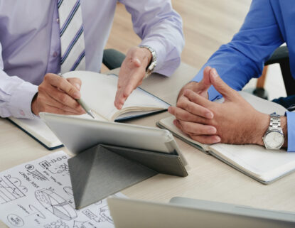 Two professionals discussing business strategy with notes, diagrams, and a tablet during a planning session.