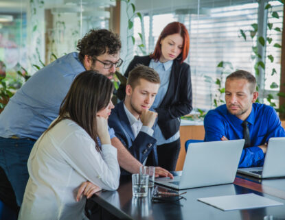 Business development team collaborating around laptops in a modern office setting.